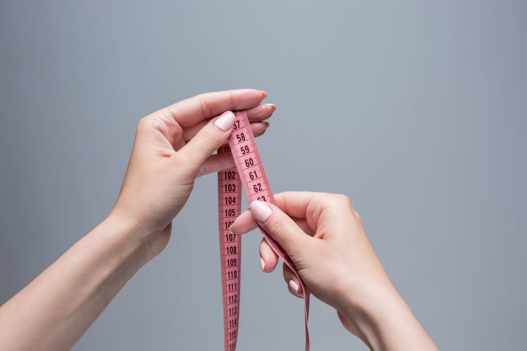 ženské ruky držia textilný meter, vhodný aj na meranie penisu. 